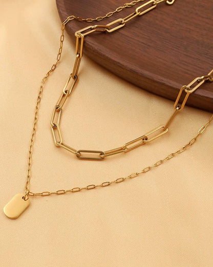 Gold chain necklace with a tag on a beige surface.