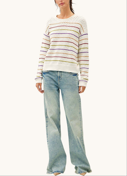 A woman modeling a cream knit sweater with thin multicolored horizontal stripes and light-wash wide-leg jeans against a plain off-white background.