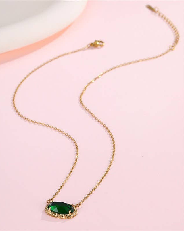 Gold necklace with a green gemstone pendant on a pink background.
