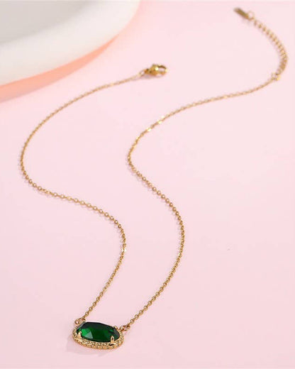 Gold necklace with a green gemstone pendant on a pink background.