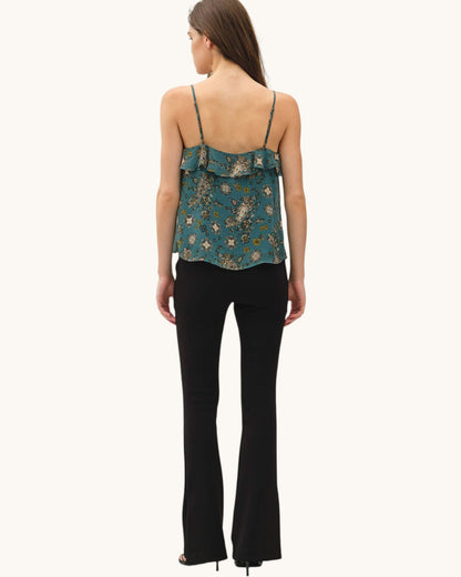 A woman shown from the back wearing a teal floral spaghetti-strap camisole top and black flared pants against a plain off-white background.