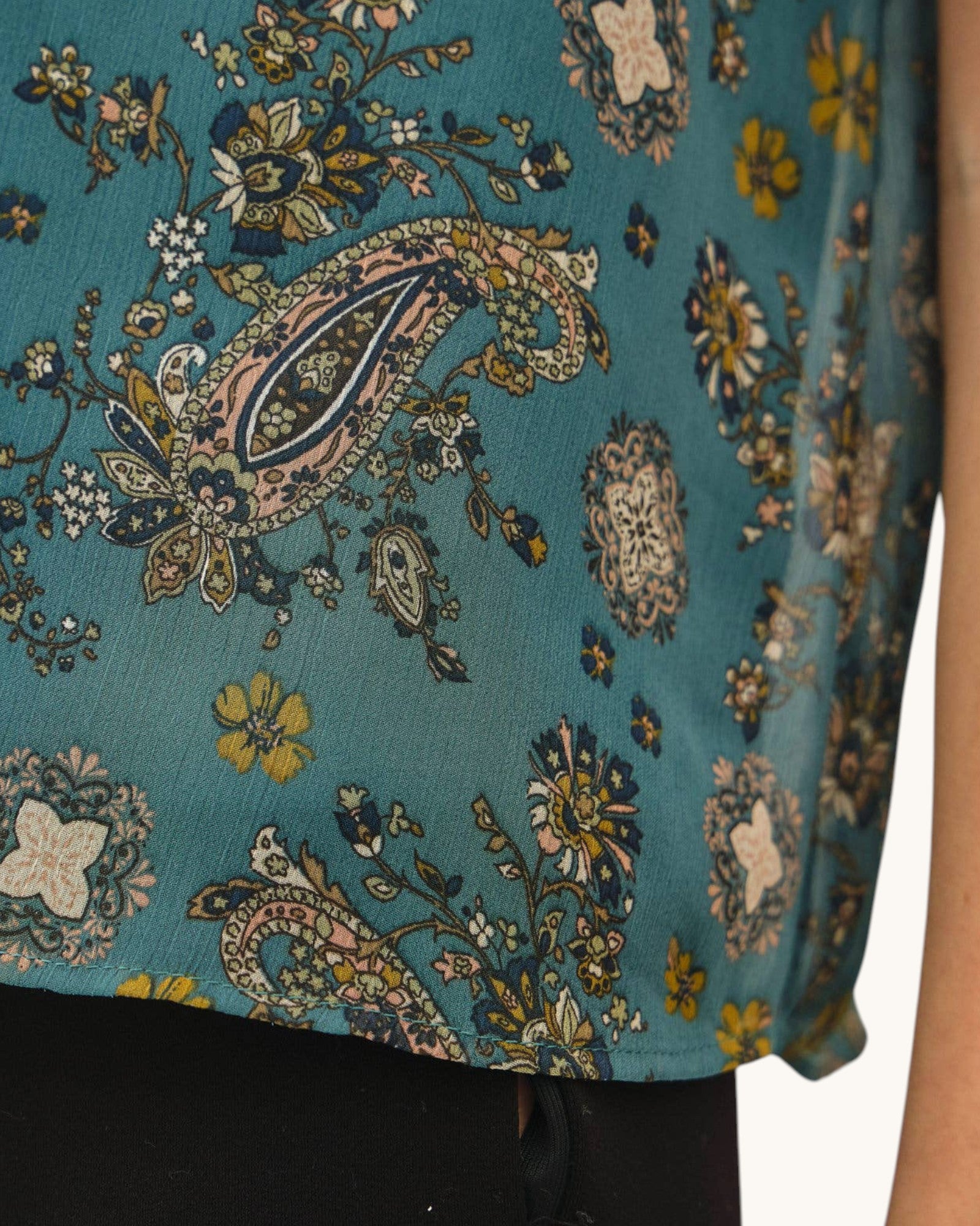 Close-up of a sleeveless top with a teal blue paisley and floral print, featuring yellow, beige, and navy details, worn by a model.