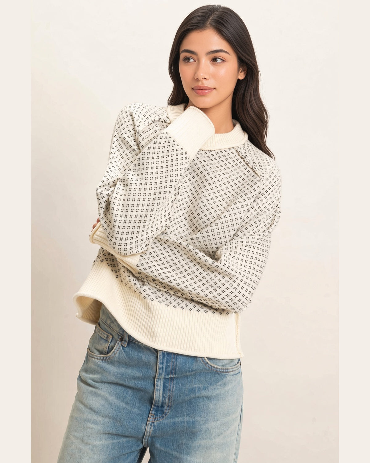Model wearing cream birdseye knit sweater with charcoal pattern and long sleeves, arms crossed.
