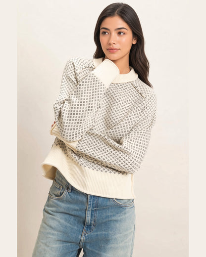 Model wearing cream birdseye knit sweater with charcoal pattern and long sleeves, arms crossed.
