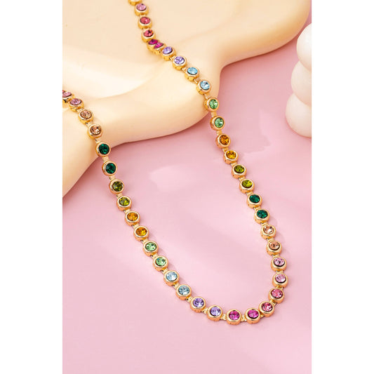 Multicolored gemstone and gold necklace on a pink surface.