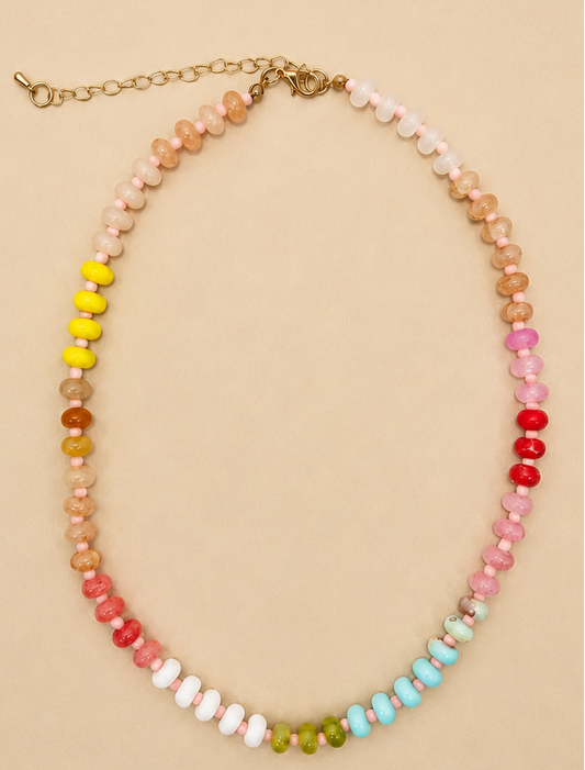 A beaded necklace with faceted round beads in a rainbow gradient, featuring a gold-tone chain clasp, displayed on a solid beige background.