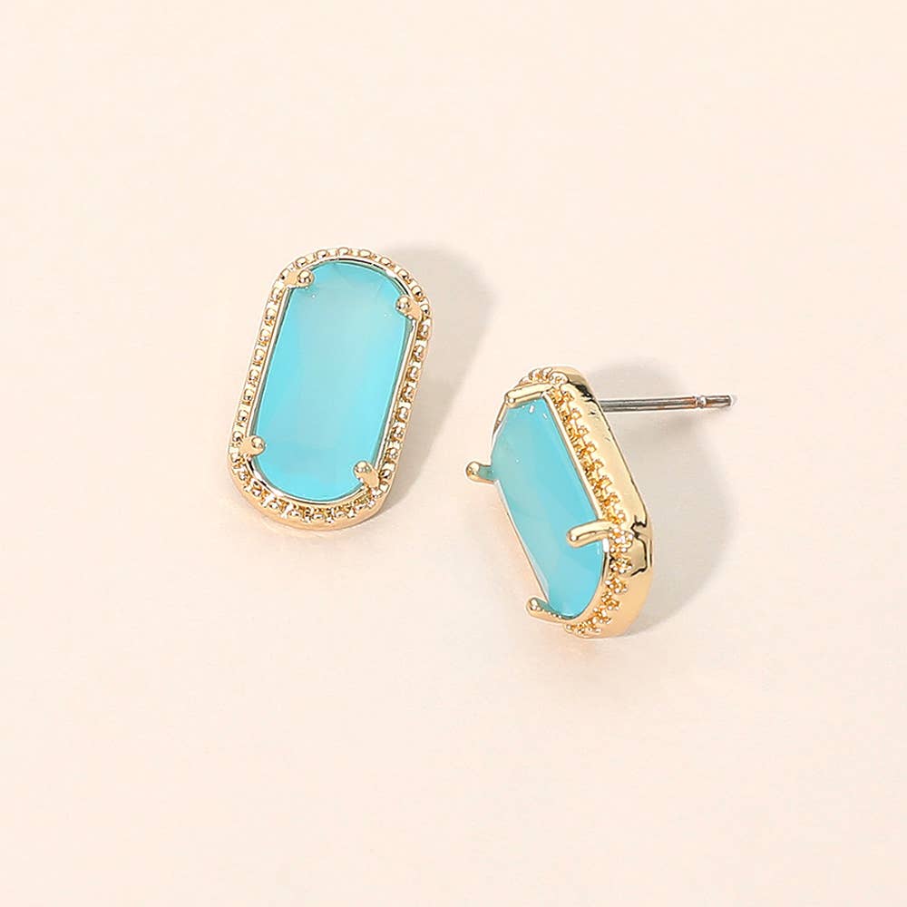 Pair of gold stud earrings with oversized teal blue crystal gemstones on a beige background.