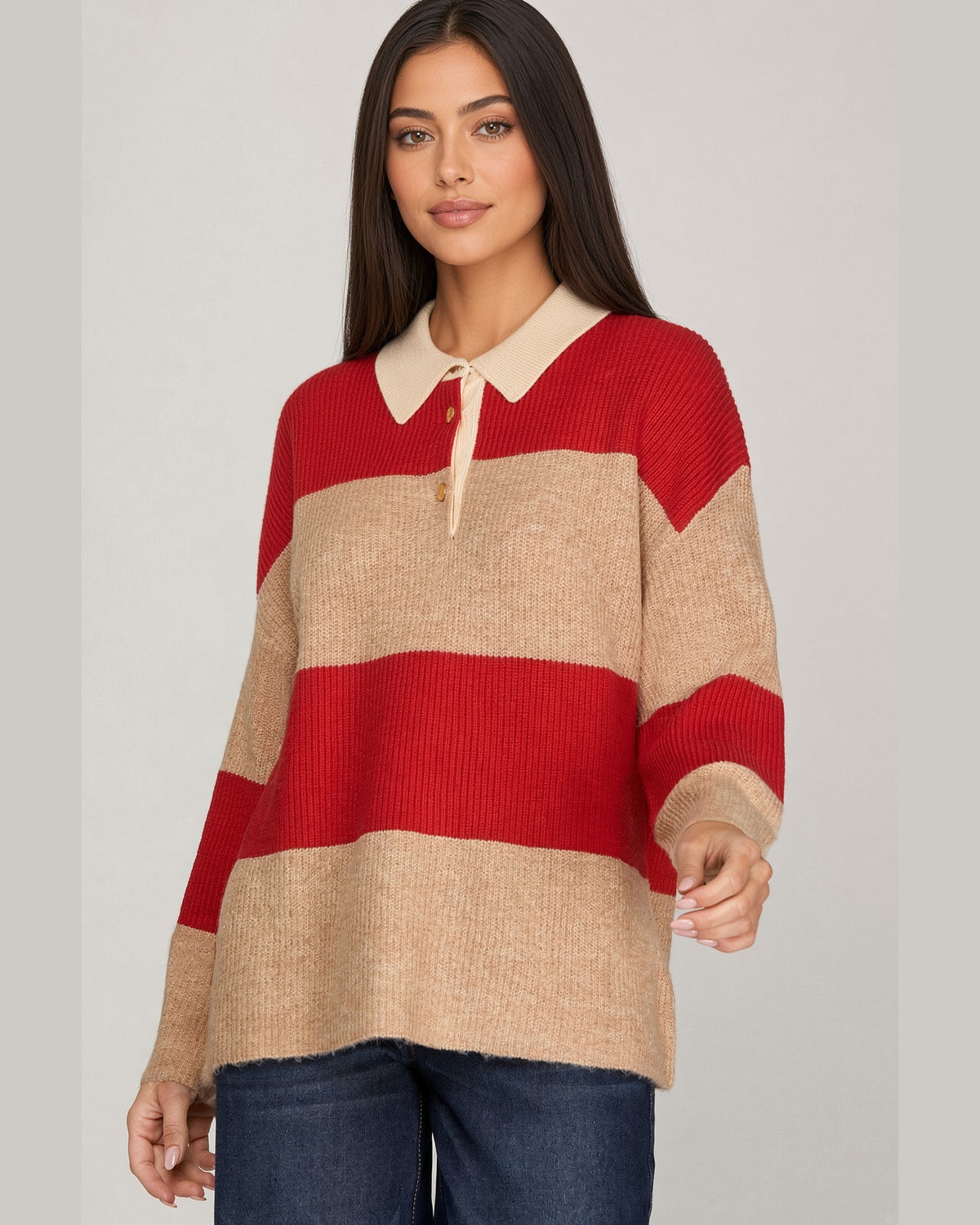 A woman modeling a knit sweater with wide horizontal stripes in red and beige, featuring a cream-colored collar with gold snap buttons, set against a plain light gray studio background.