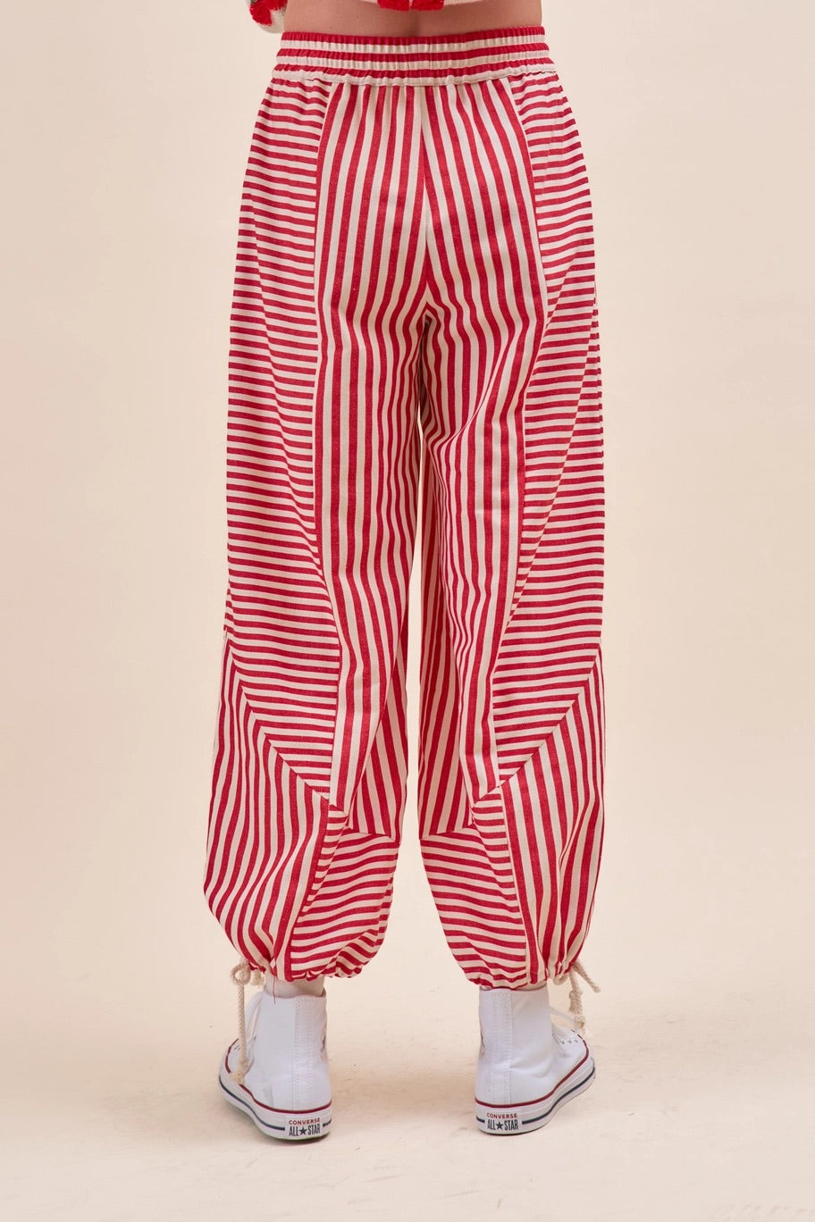 Red and white vertically striped harem pants with drawstring ankle cuffs, shown on a model from the back.