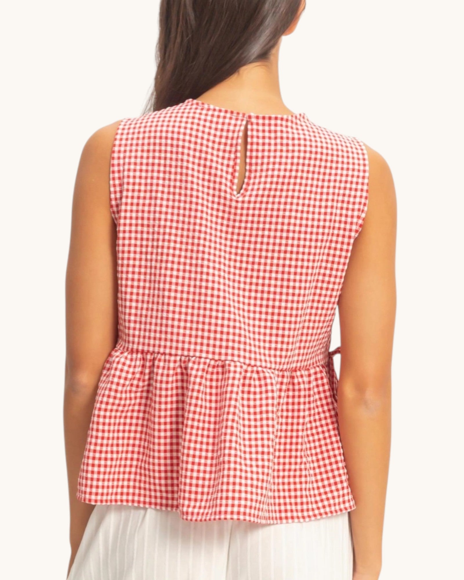 Red and white checkered sleeveless top worn by a person on a white background