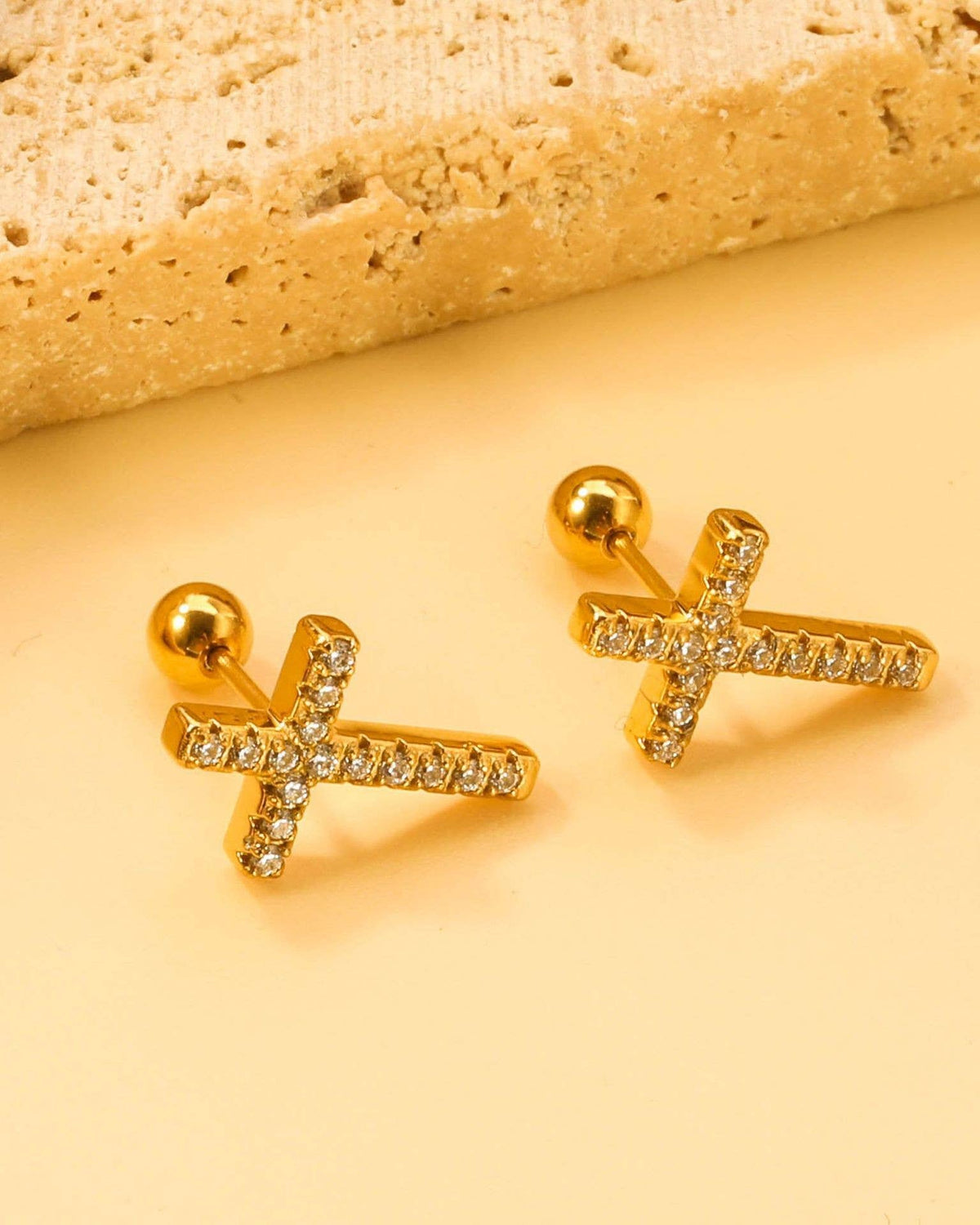 Gold earrings with rhinestone accents on a yellow background.