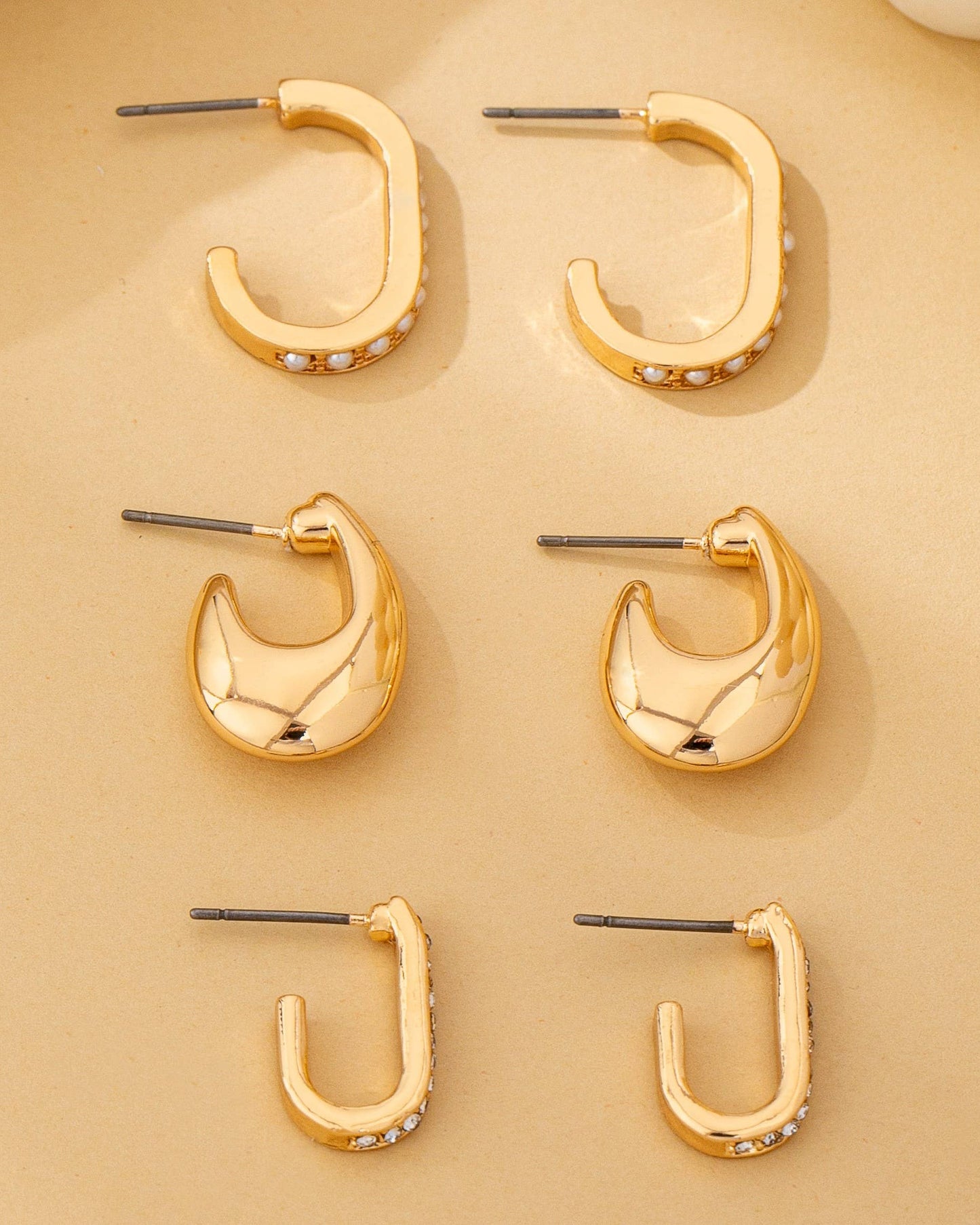 Set of 3 gold hoop earrings on a beige background.
