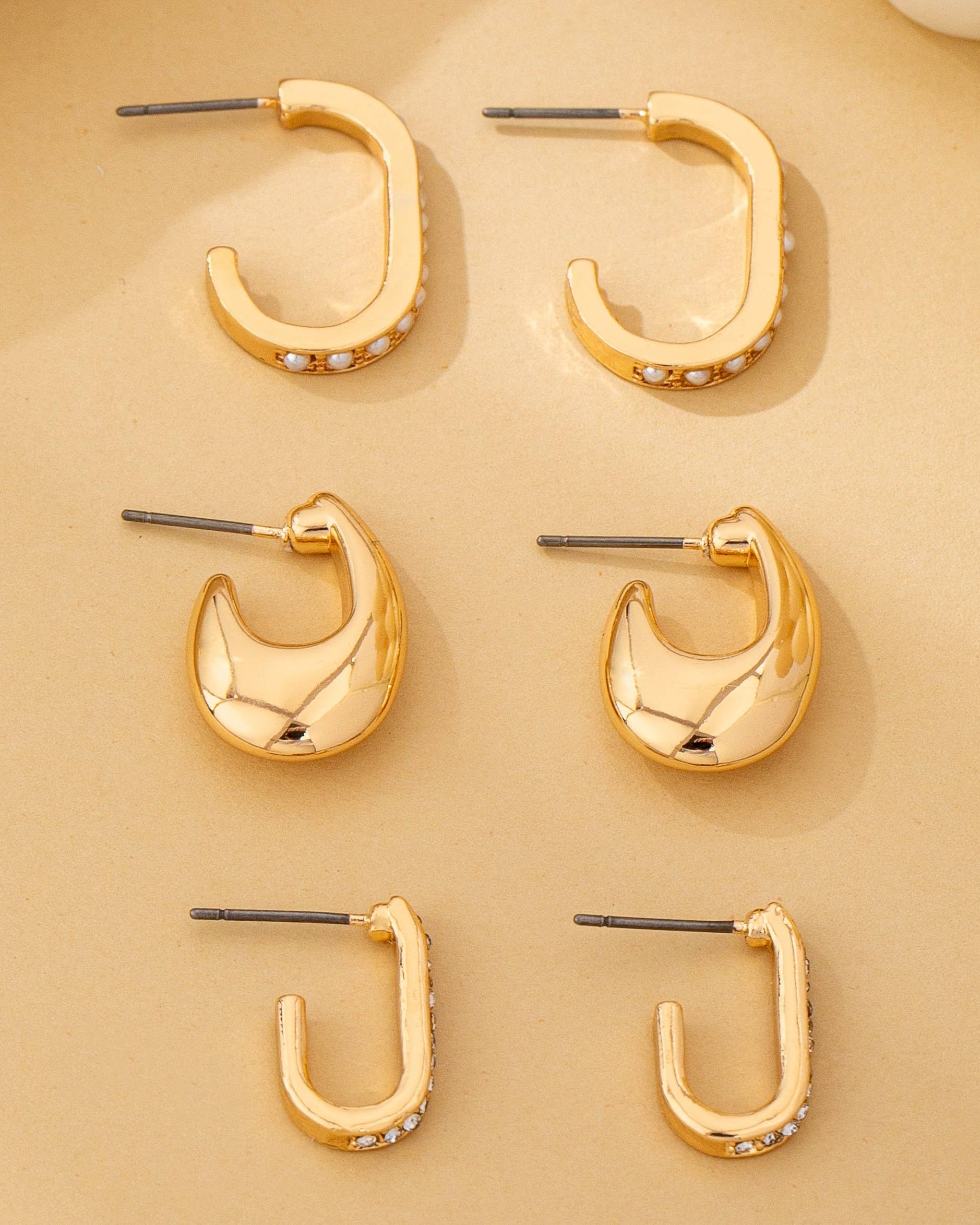 Set of 3 gold hoop earrings on a beige background.