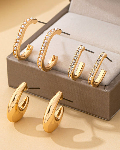 3 different sets of Gold hoop earrings with embedded stones on a beige surface and display box.