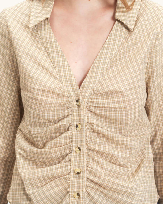 Close-up of a beige and white checkered button-up shirt with ruched detailing and buttons, worn by a model.