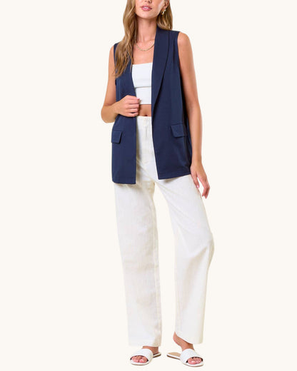 Woman wearing a navy sleeveless blazer over a white outfit on a white background.