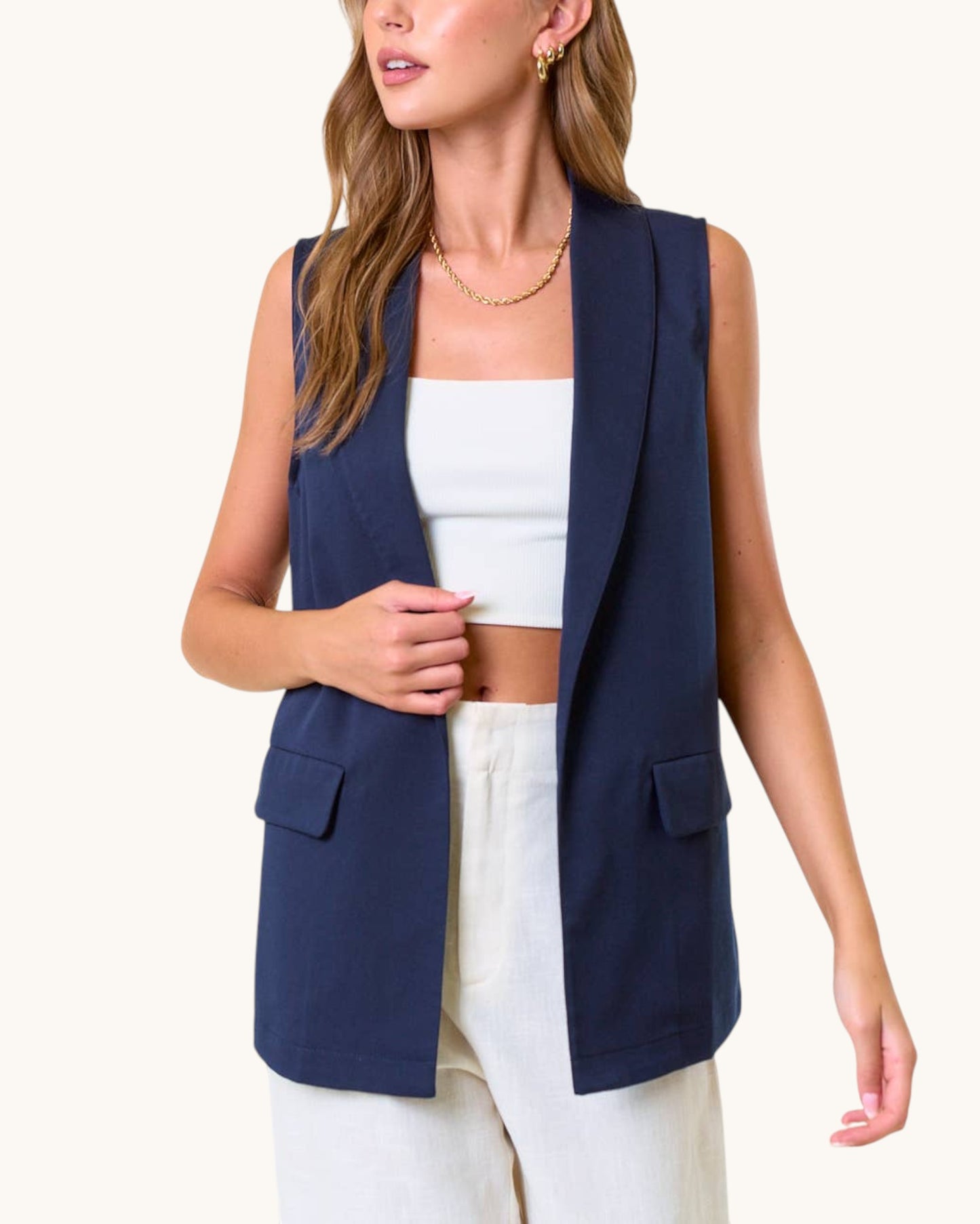 Woman wearing a navy blue open drape vest over a white top and pants on a white background.