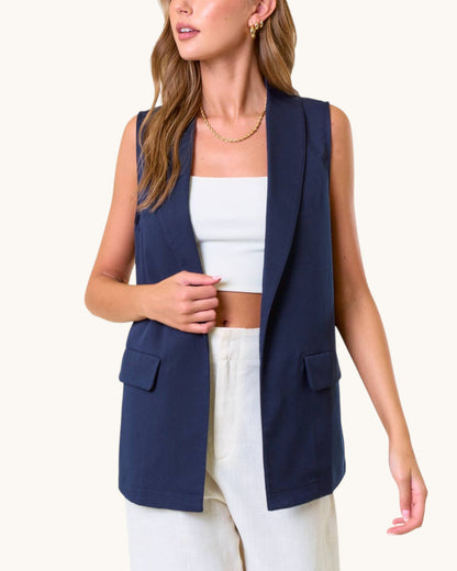 Woman wearing a navy blue open drape vest over a white top and pants on a white background.