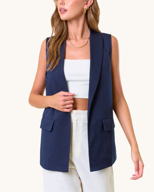 Woman wearing a navy blue open drape vest over a white top and pants on a white background.