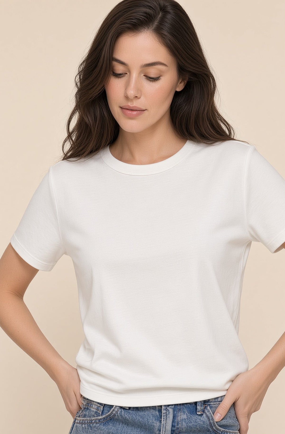 A woman wearing a plain white short-sleeve crewneck t-shirt and blue jeans, standing against a solid beige background.
