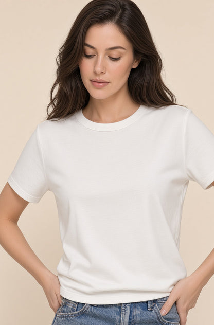 A woman wearing a plain white short-sleeve crewneck t-shirt and blue jeans, standing against a solid beige background.