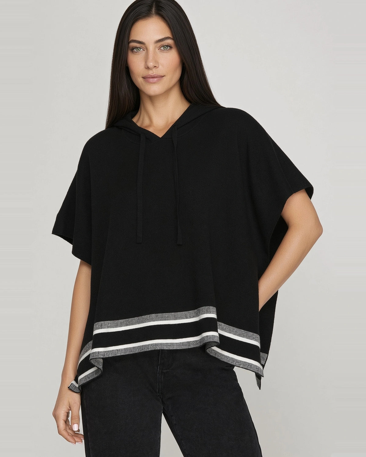 Front view of black short sleeve knit hoodie cape showing drawstring hood, relaxed fit, and gray and white striped hem.