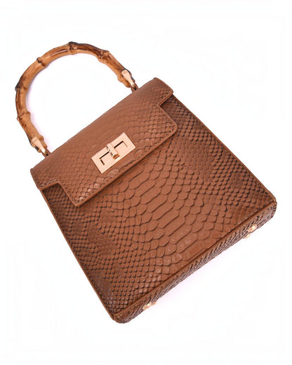 A brown snakeskin textured handbag with a bamboo handle and a gold-tone logo clasp on the front flap, photographed on a white background.