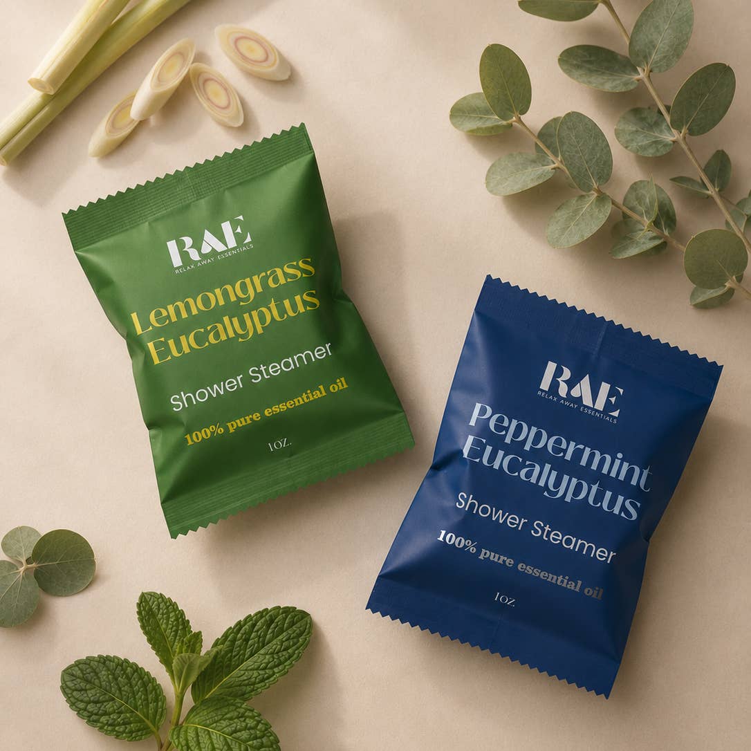 Two shower steamer packets, one green and one blue, with RAE branding on a light background with greenery.