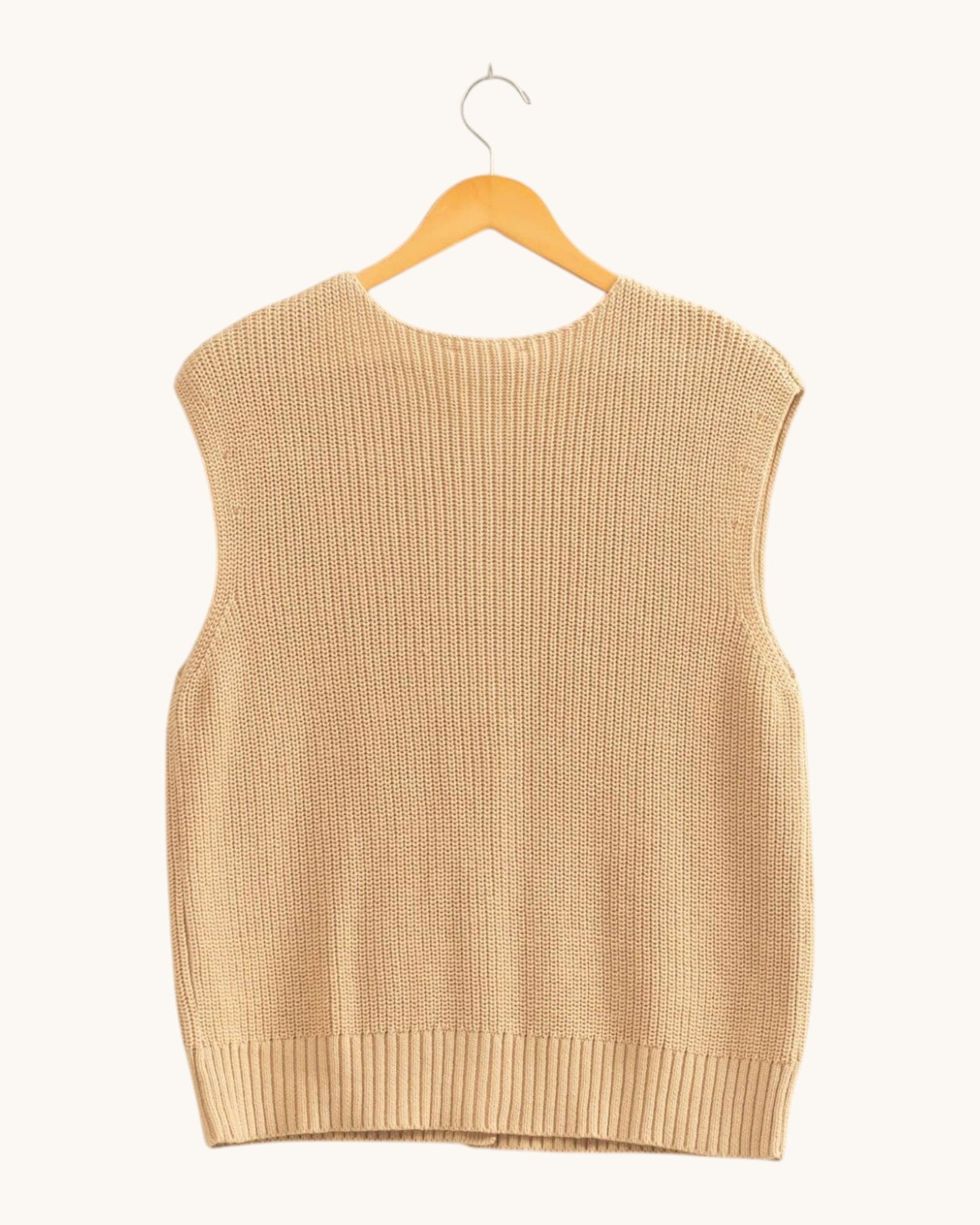 Back view of a sleeveless ribbed knit sweater vest in a warm beige color, hanging on a wooden hanger against a solid off-white background.