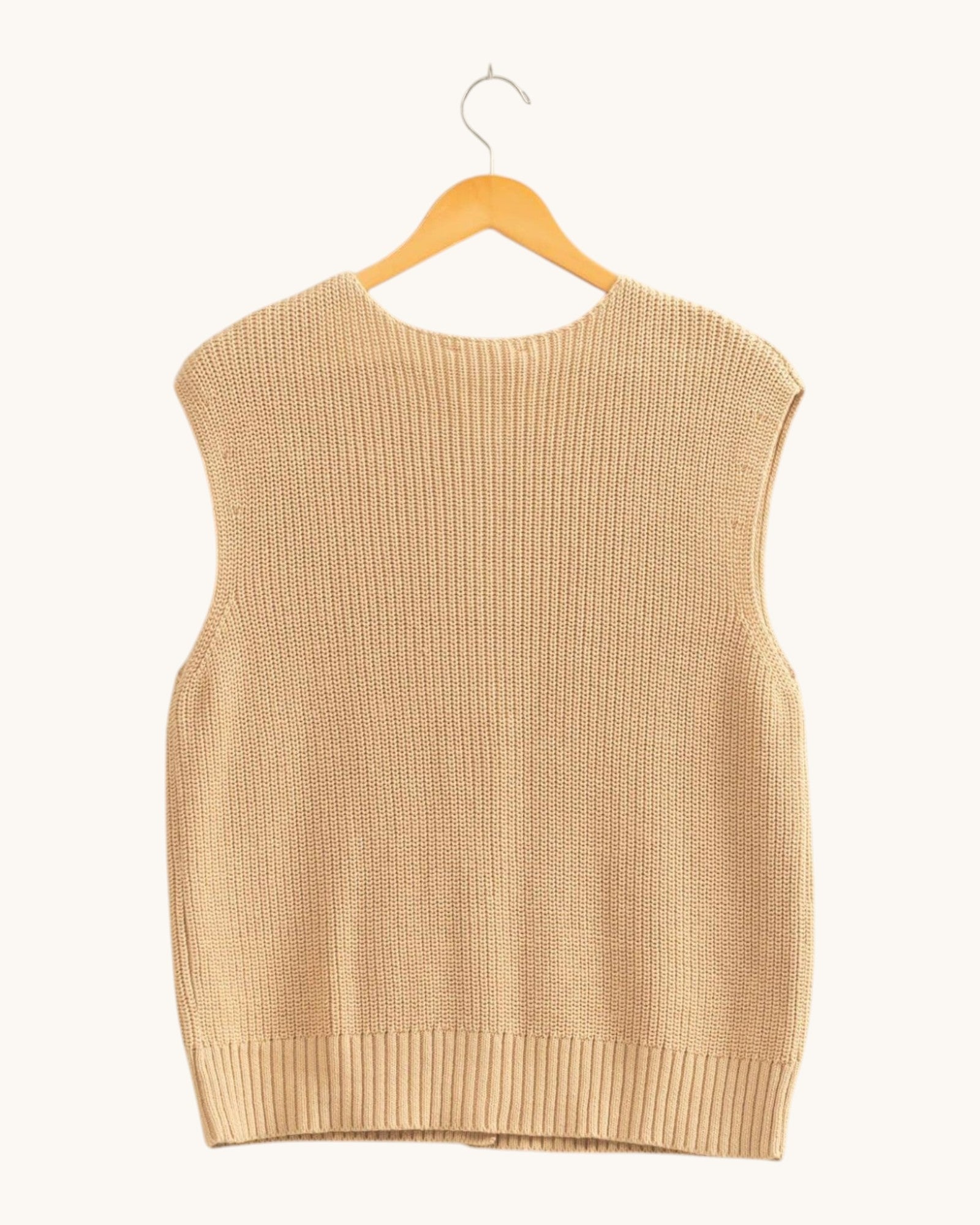 Back view of a sleeveless ribbed knit sweater vest in a warm beige color, hanging on a wooden hanger against a solid off-white background.