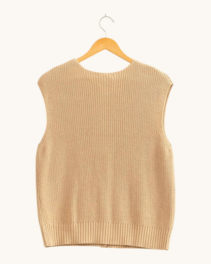 Back view of a sleeveless ribbed knit sweater vest in a warm beige color, hanging on a wooden hanger against a solid off-white background.