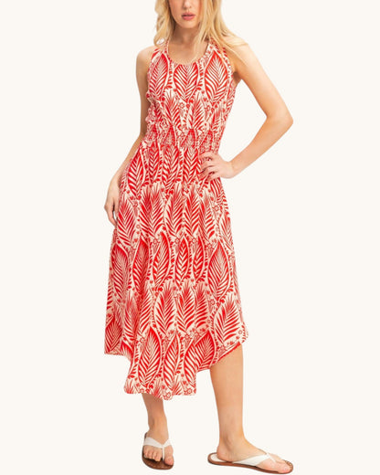 A woman modeling a sleeveless midi dress with a red and white palm leaf pattern, paired with white slide sandals, against a solid off-white background.