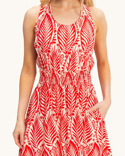 A sleeveless halter-neck dress with a red and white palm leaf pattern, featuring a smocked waist and side pockets, shown on a model against a light background.