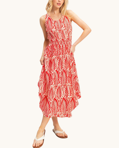 A woman modeling a sleeveless midi dress with a red and white leaf pattern, paired with white slide sandals, against a plain off-white background.