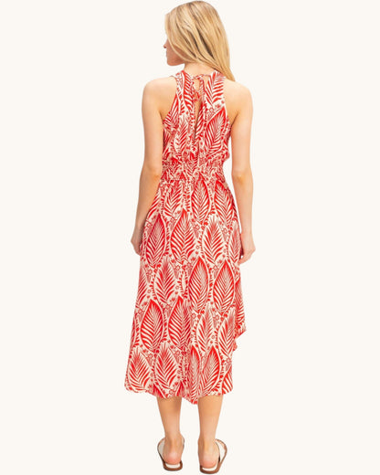 A woman viewed from the back wearing a sleeveless midi dress with a red and white palm leaf pattern, set against a plain off-white background.