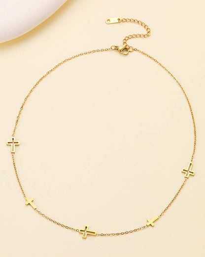 A delicate gold chain necklace featuring five small cross pendants spaced evenly along the chain, displayed on a light beige background.