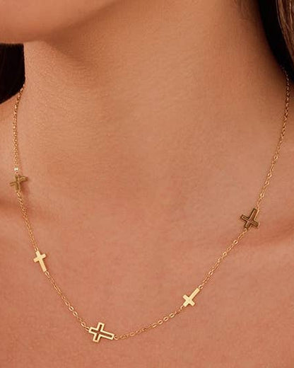 A delicate gold chain necklace with five small cross charms spaced along the chain, shown worn on a model's neck.