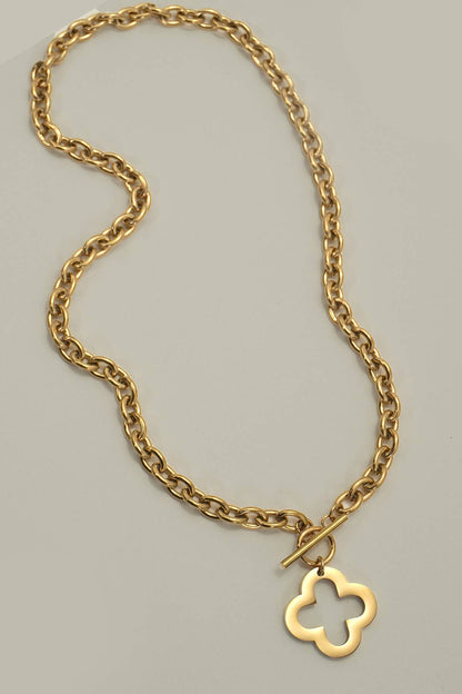 A gold chain necklace with a toggle clasp and an openwork four-leaf clover pendant, photographed on a plain light gray background.