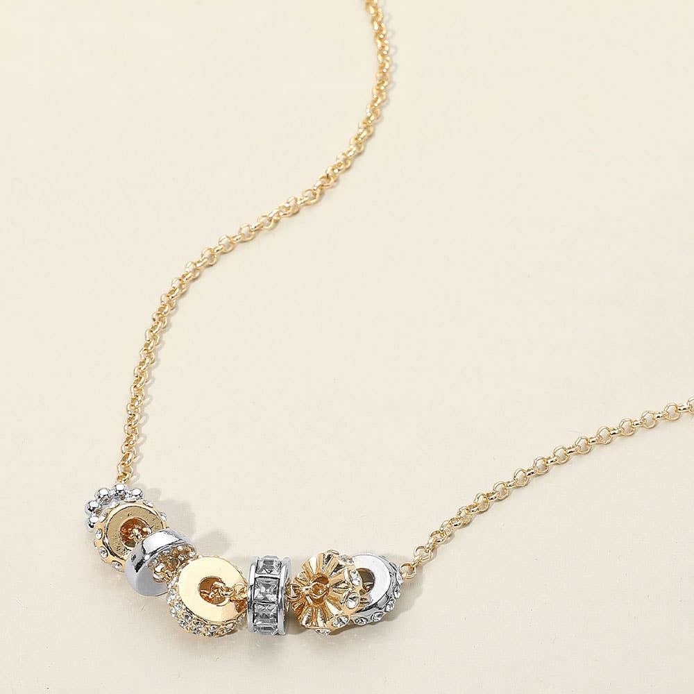 Gold necklace with  gold and silver circular pendants on a beige background.