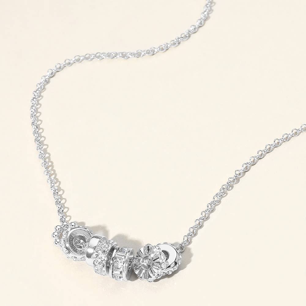 Silver necklace with circular pendants on a light beige background.