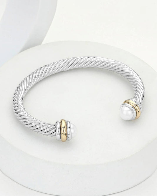Silver twisted rope cuff bracelet with white pearl tips and gold accent rings displayed on a white pedestal.