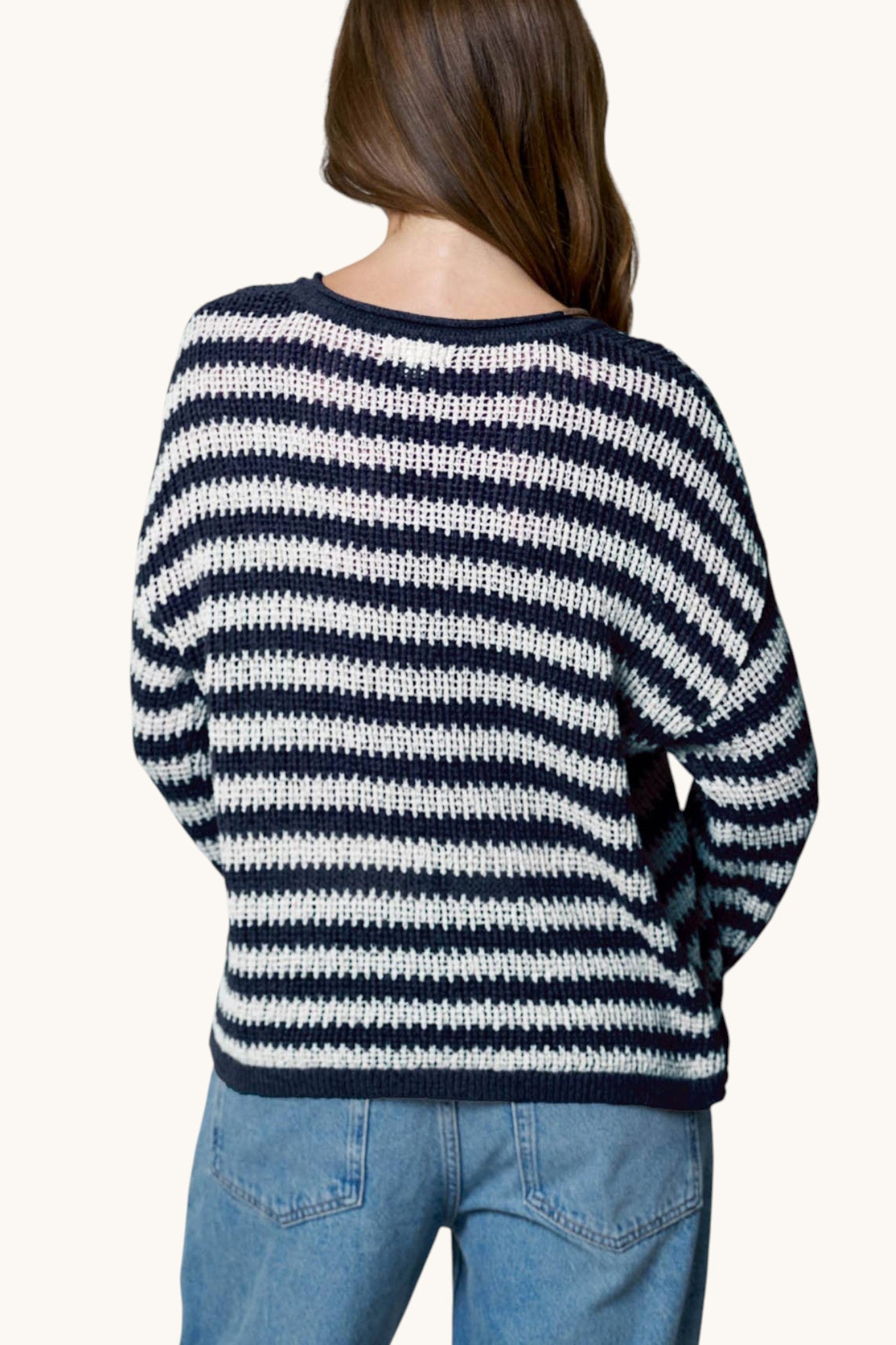 A woman viewed from behind wearing a navy and white horizontally striped knit sweater and blue jeans against a plain light background.