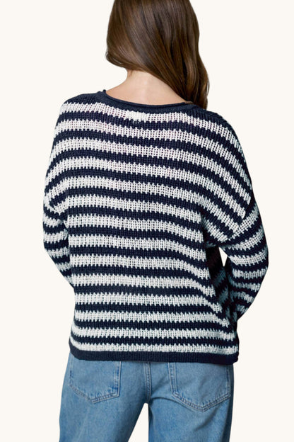 A woman viewed from behind wearing a navy and white horizontally striped knit sweater and blue jeans against a plain light background.