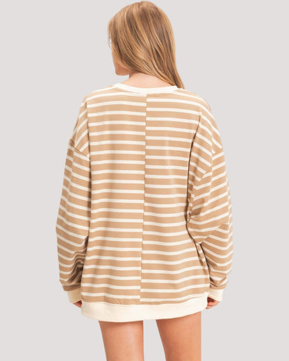 A woman viewed from the back wearing a loose, long-sleeve striped sweatshirt with horizontal beige and off-white stripes, set against a solid light gray background.