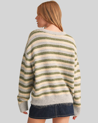 A woman shown from the back wearing a fuzzy knit sweater with horizontal stripes in olive green, blue-gray and cream, paired with a dark denim mini skirt, against a solid light gray background.