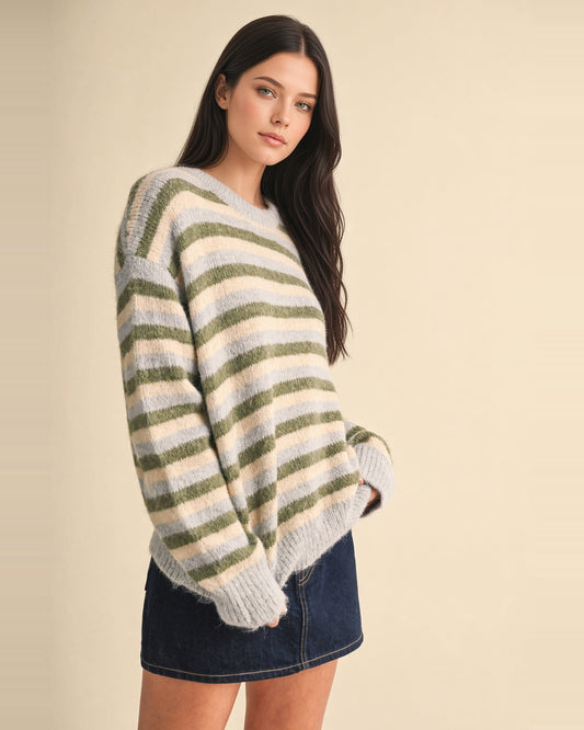 A dark haired woman wearing a fuzzy knit crewneck sweater with horizontal stripes in sage green, cream, and light gray-blue, posed against a solid beige studio background.