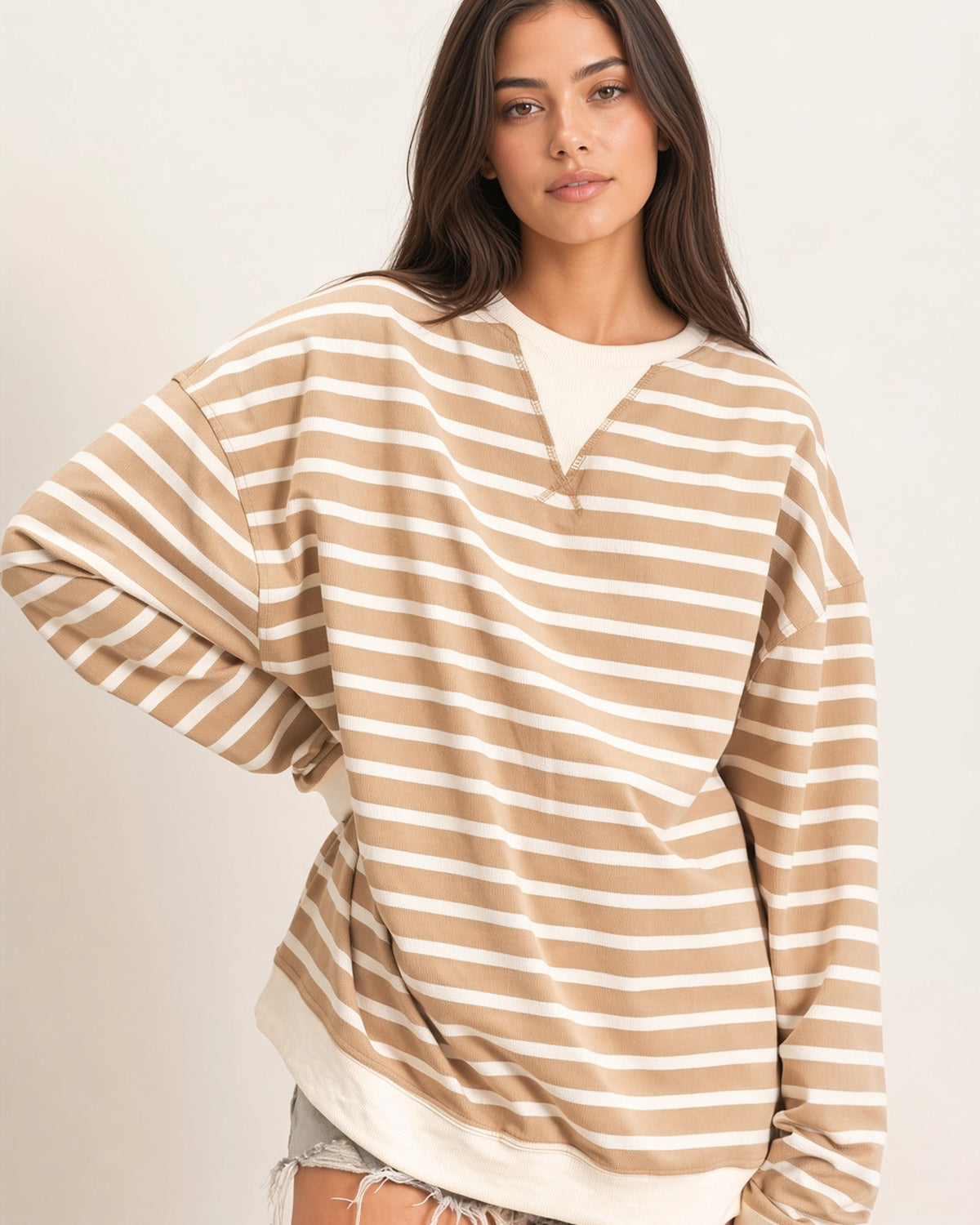 A woman wearing an oversized beige and off-white horizontally striped long-sleeve knit top with contrasting ribbed ivory neckline and hem/cuffs. 