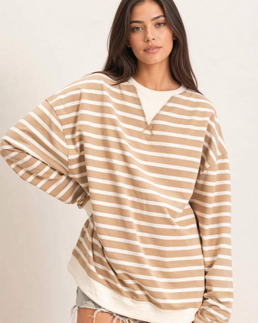 A woman wearing an oversized beige and off-white horizontally striped long-sleeve knit top with contrasting ribbed ivory neckline and hem/cuffs. 