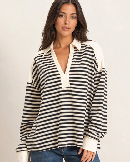 A woman wearing a long-sleeve polo-style sweatshirt top with horizontal black and cream stripes, cream shoulder panels, and a cream collar, paired with blue jeans against a plain light background.