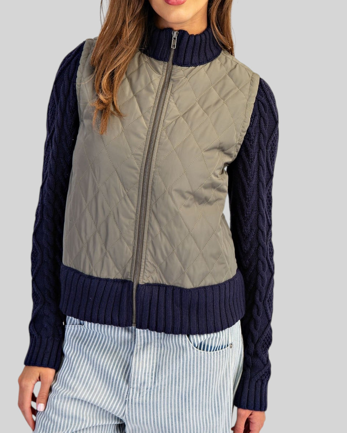 Navy and olive mixed-media jacket with quilted body, navy cable knit sleeves, and ribbed trim with a zipper front.